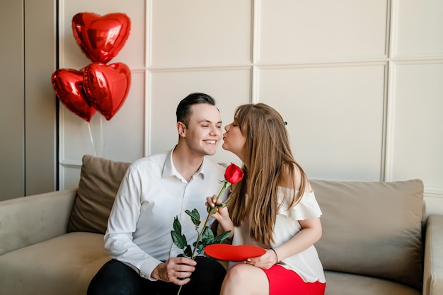 Hombre y mujer en casa en el sofá con rosa roja y tarjeta de San Valentín en forma de corazón