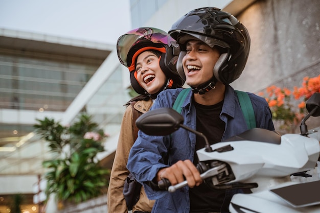 un hombre y una mujer con casco riéndose mientras conducen una motocicleta