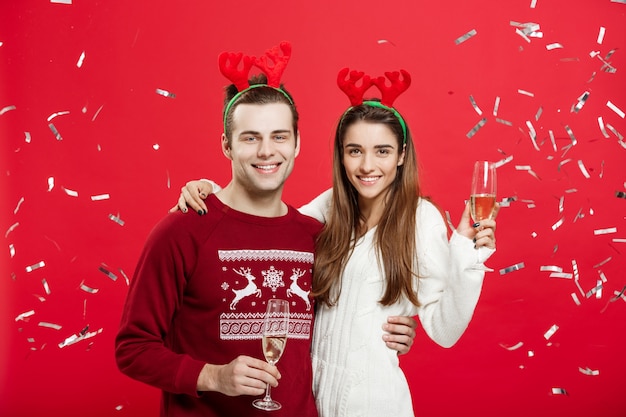 Hombre y mujer caucásicos felices en los sombreros del reno que celebran la Navidad que tuesta con las flautas de champán, felicitando en Navidad.
