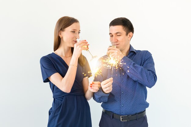 Hombre y mujer celebrando la fiesta de Navidad o año nuevo con luces de Bengala y copas de champán sobre fondo blanco.