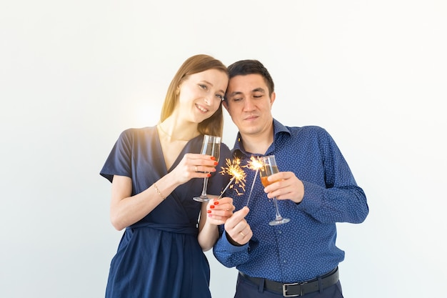 Hombre y mujer celebrando la fiesta de Navidad o año nuevo con luces de Bengala y copas de champán sobre fondo blanco.