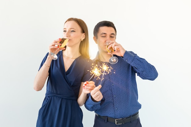 Hombre y mujer celebrando la fiesta de Navidad o año nuevo con luces de Bengala y copas de champán sobre fondo blanco.