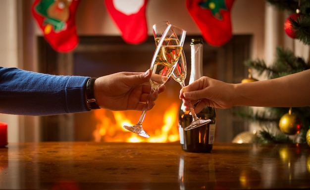 Hombre y mujer cenando y tintineando vasos junto a la chimenea encendida