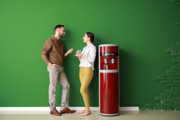 Hombre y mujer cerca del enfriador de agua contra la pared de color