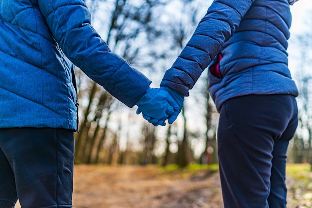 Hombre y mujer en chaquetas azules y guantes de látex caminando en el parque. Amor pareja cogidos de la mano en el parque.