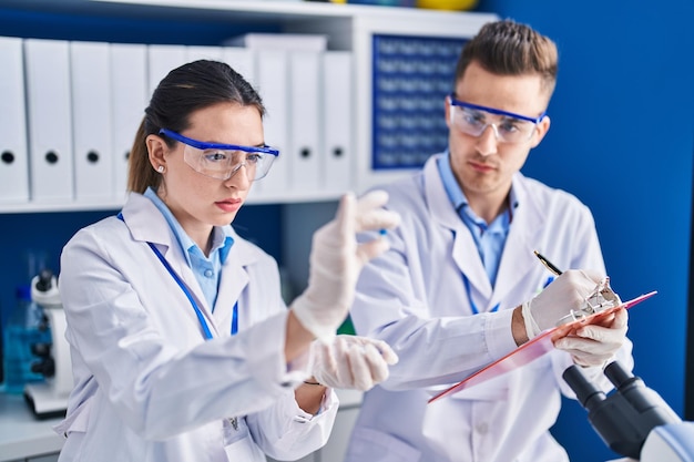 Un hombre y una mujer científicos con pastillas escriben en un documento en el laboratorio.