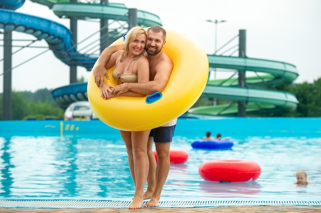 Un hombre y una mujer en un círculo inflable de goma están parados contra el fondo de una piscina de un parque acuático de verano.