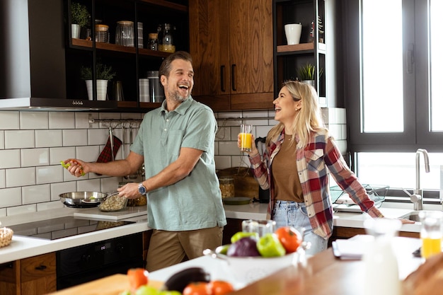 Hombre y mujer compartiendo una risa mientras cocinan en una cocina acogedora y bien organizada