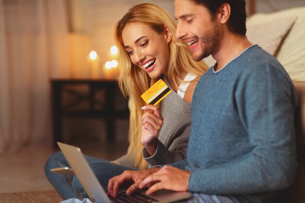 Hombre y mujer comprando en línea con portátil y tarjeta de crédito comprando cosas en Internet en el interior