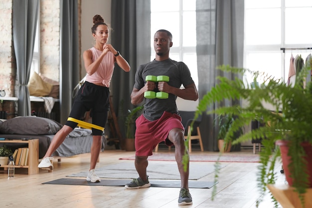 Hombre y mujer deportivos haciendo ejercicios de fortalecimiento en la sala de loft usando banda de resistencia y pesas