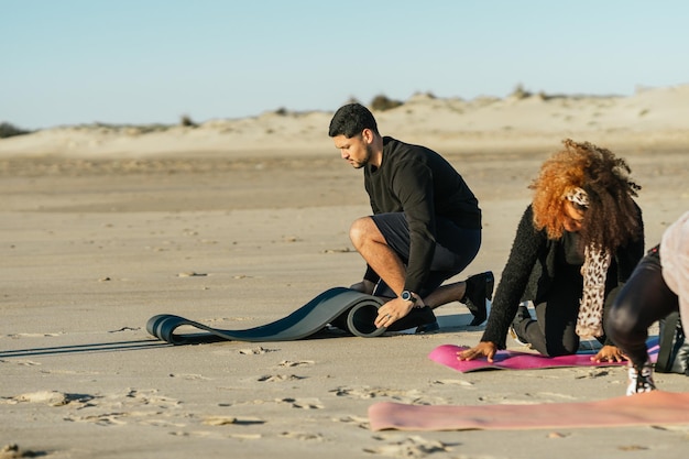 El hombre y la mujer desplegando una estera de yoga en la arena de la playa
