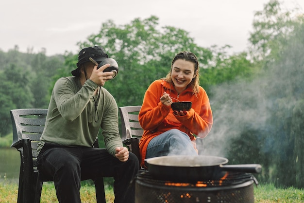 Un hombre y una mujer disfrutan de la comida junto al fuego Campamento de senderismo con una hoguera en el bosque Turista en recreación fuera de Campamento estilo de vida