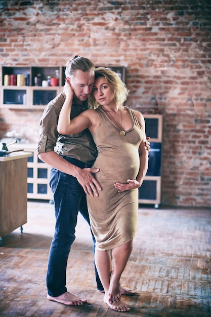 Hombre y mujer embarazada bailan junto a la ventana en la sala de estilo loft