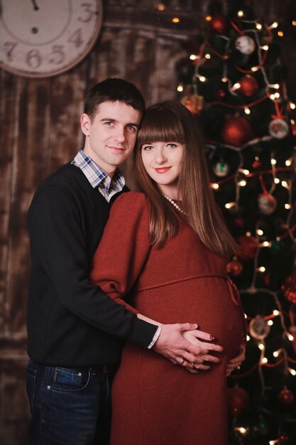 Hombre y mujer embarazada posando cerca del árbol de Navidad