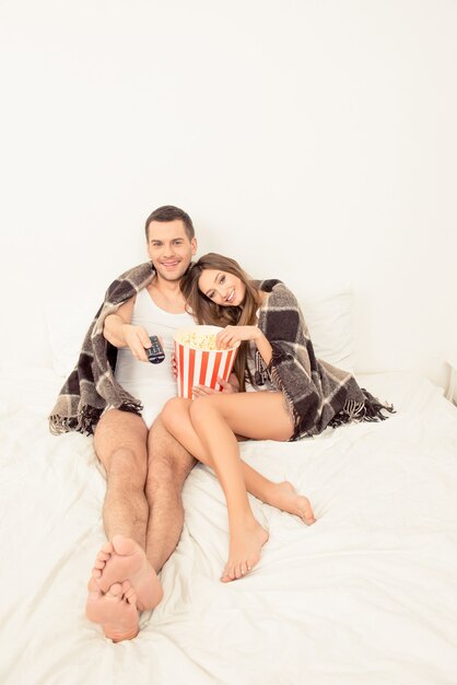 Hombre y mujer enamorados viendo la película con palomitas de maíz en la cama