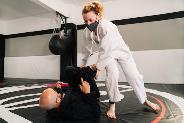 Hombre y mujer entrenando artes marciales y judo con kimonos en la alfombra del piso del gimnasio con una mascarilla debido al covid 19