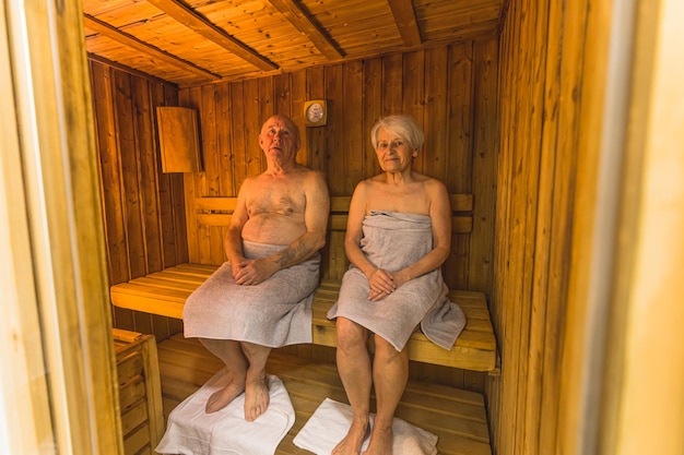 Hombre y mujer envejecidos en la sauna de madera mirando a la cámara satisfechos con la toma completa