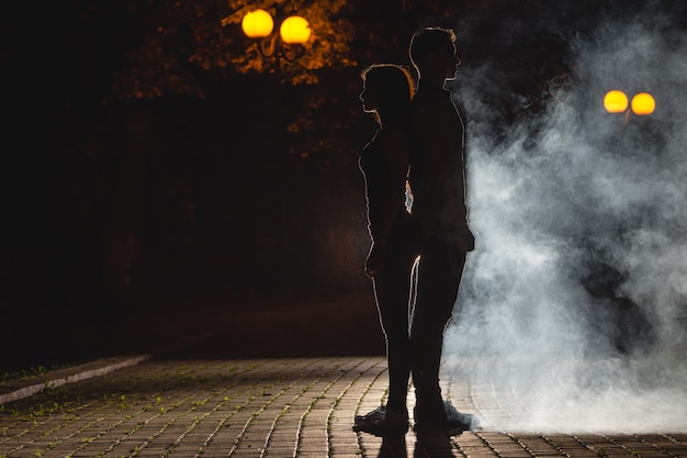 El hombre y la mujer están parados en la calle oscura sobre un fondo de humo. Noche