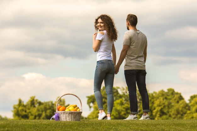 El hombre y la mujer están parados en la hierba cerca de una canasta con frutas.