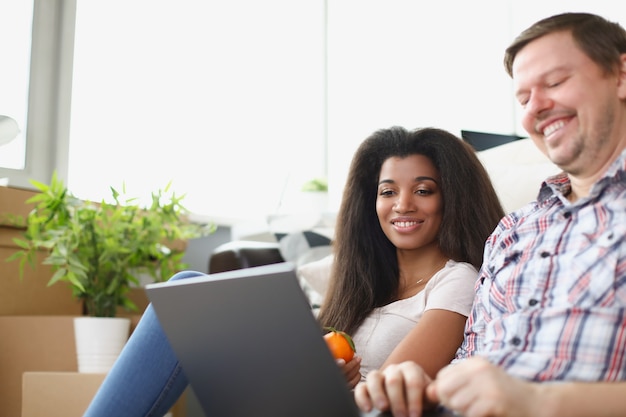 El hombre y la mujer están sentados en el suelo y mirando la computadora portátil