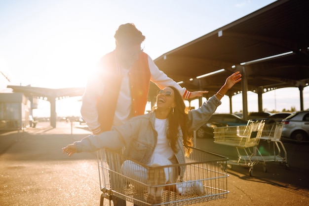 Hombre y mujer con estilo divirtiéndose y montando carrito de compras Concepto juvenil de ocio de estilo de vida