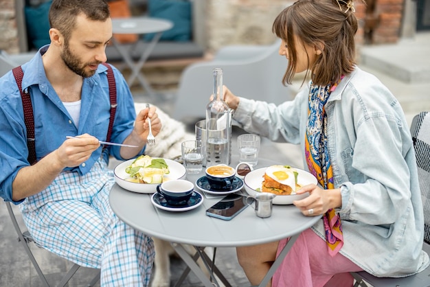 El hombre y la mujer con estilo tienen un delicioso desayuno en la cafetería al aire libre