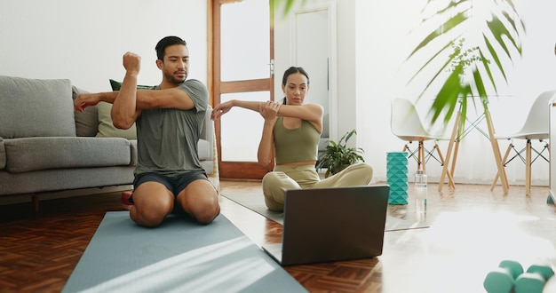 Hombre y mujer estirándose con computadora portátil clase en línea y calentarse para hacer ejercicio y entrenamiento muscular en casa entrenamiento video en internet y pareja con deportes bienestar y tecnología para guía de salud