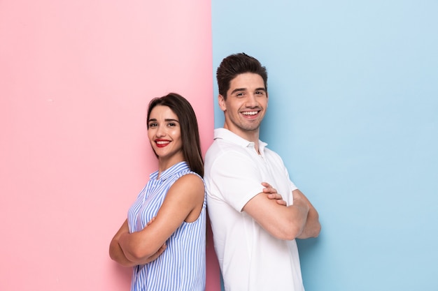 Hombre y mujer europeos en ropa casual de pie espalda con espalda con los brazos cruzados, aislado sobre la pared colorida