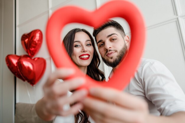 Hombre y mujer con forma de corazón en las manos mirando a través de su casa con globos