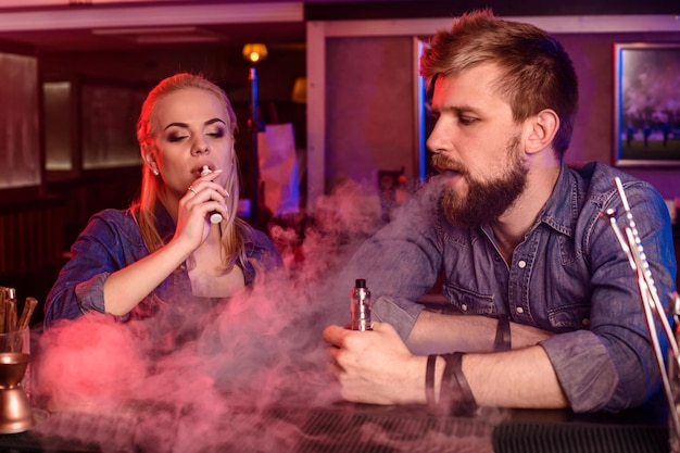 Un hombre y una mujer fumando cigarrillos electrónicos en un bar de vape.