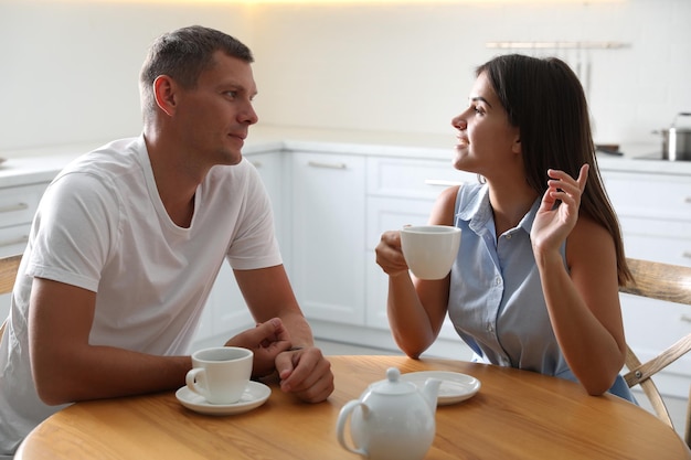 Hombre y mujer hablando mientras beben té en la mesa en la cocina