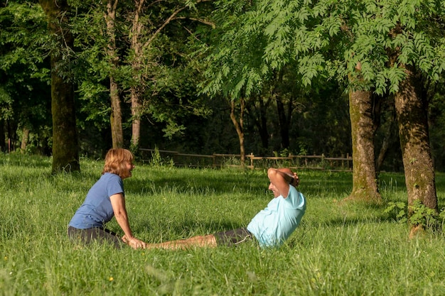 Hombre y mujer haciendo sentadillas juntos y ayudándose rodeados de naturaleza