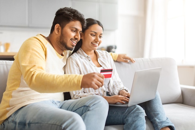 Hombre y mujer indios sentados en el sofá comprando con una computadora portátil