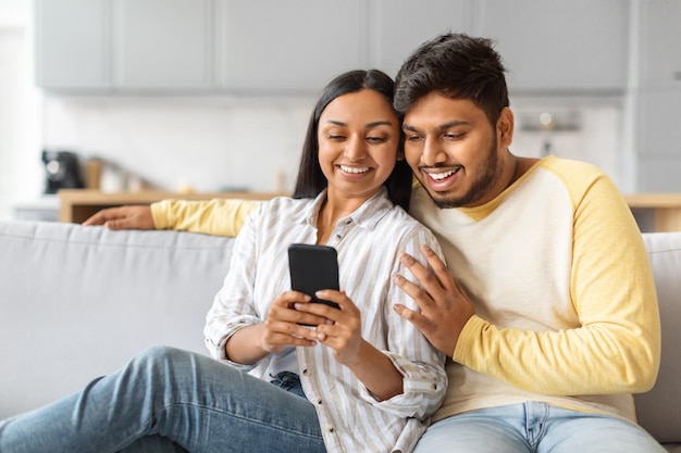 Hombre y mujer indios sentados en el sofá mirando el teléfono celular