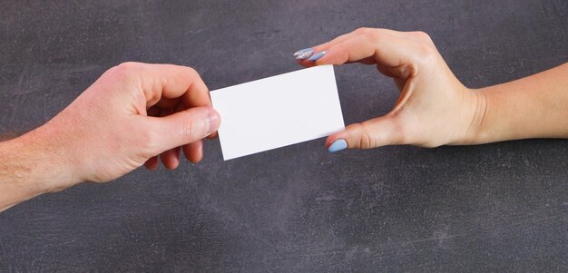 Un hombre y una mujer intercambian tarjetas de visita. Vista de cerca de las manos. Fondo de piedra gris.