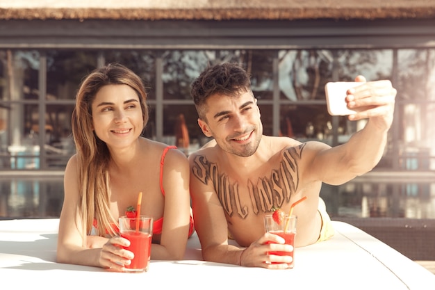 Hombre y mujer joven descansan juntos junto a la piscina tomando fotos