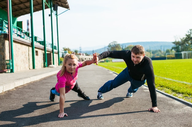 Foto hombre y mujer joven haciendo ejercicio de flexión de brazos y tocando las palmas en el estadio