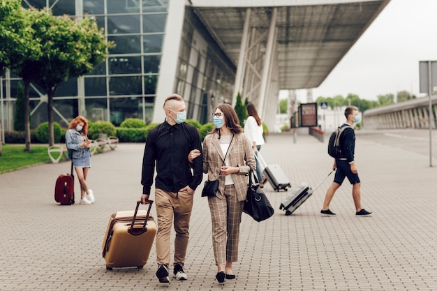 Hombre y mujer joven con máscaras protectoras con una maleta van al aeropuerto