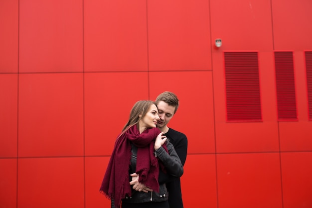 Hombre y mujer joven con pasión, emoción, en la calle con un telón de fondo de la pared roja. Moda