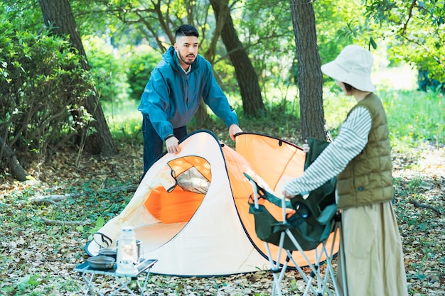 Hombre y mujer joven preparando tiendas de campaña para acampar en el bosque