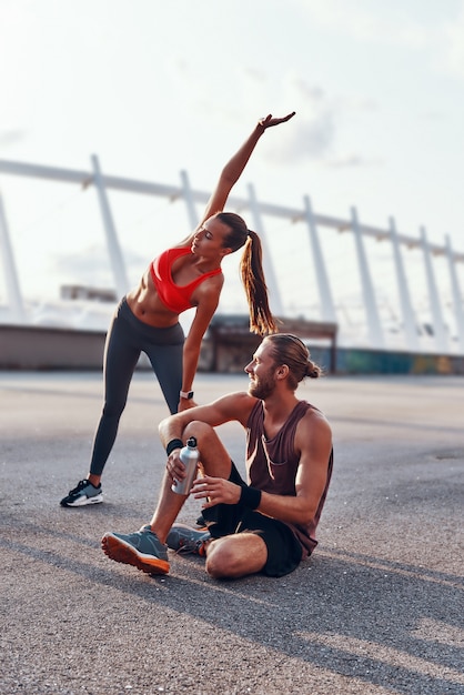 Hombre y mujer joven en ropa deportiva calentando y estirando al aire libre