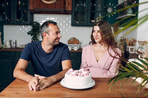 El hombre y la mujer joven se sientan en la cocina casera con la torta en la mesa.