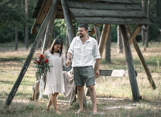 Hombre y mujer jóvenes elegantemente vestidos, con un ramo de flores exóticas, en una cita en el bosque.