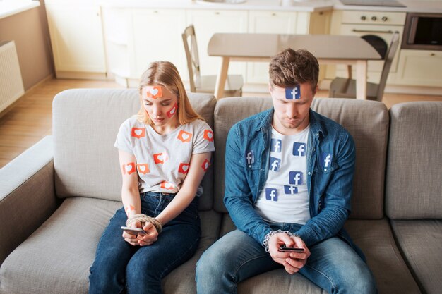 Foto el hombre y la mujer jóvenes tienen adicción a las redes sociales. atascado en los teléfonos. sentado en el sofá y mirando.