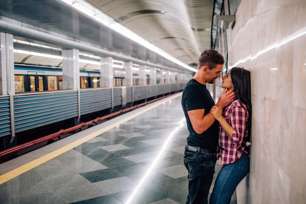 El hombre y la mujer jóvenes usan bajo tierra. Pareja en metro La gente alegre y paasionada se inclina hacia la pared. tiempo de besos Guy toma la mano de su cuello. Historia de amor. Vista urbana moderna.