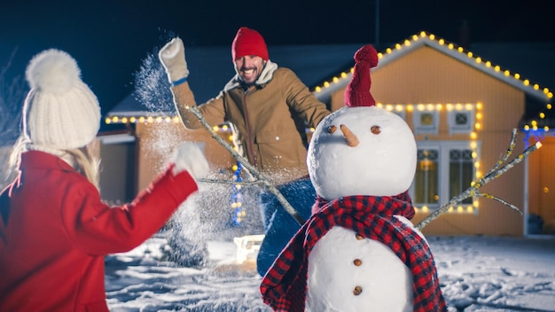 Un hombre y una mujer juegan en la nieve con un muñeco de nieve.