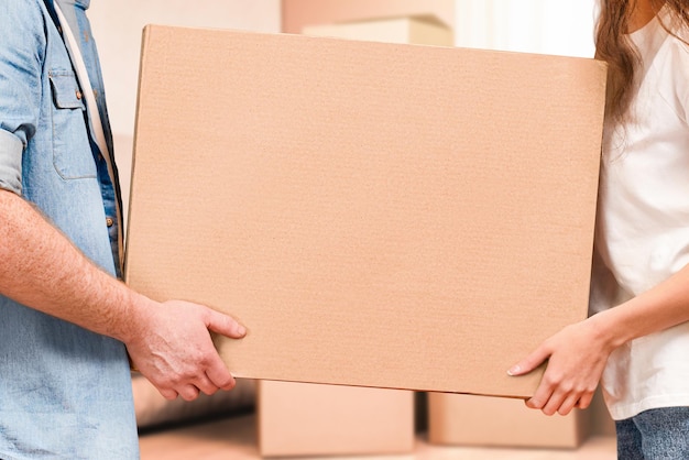 Un hombre y una mujer llevan una caja de cartón en sus manos y se mudan a una nueva casa.