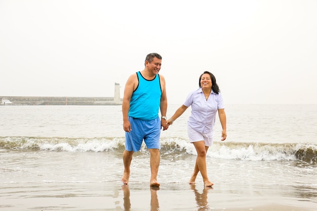 Hombre y mujer maduros de 50 años caminan en una playa felices y enamorados