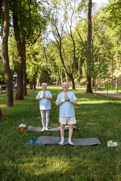 Hombre y mujer maduros con namaste hacen yoga sobre césped