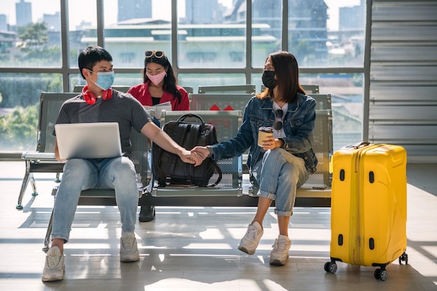 Hombre y mujer con máscara tomados de la mano sentados en el aeropuerto